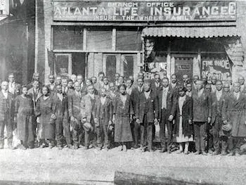 Employees and neighbors gathered outside a branch office of the Atlanta Life Insurance Company, under a sign reading Insure the Whole Family.