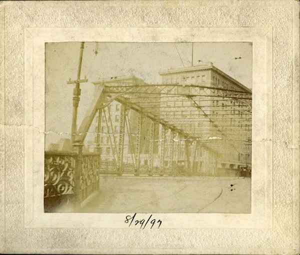 A mounted photograph of the iron truss Forsyth Street bridge in the foreground with the Austell Building behind it, 1897.