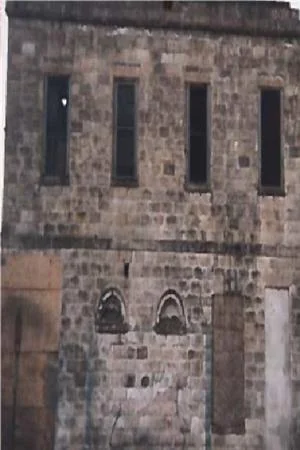 A two-story stone building with four tall, narrow upper windows and boarded openings at street level.