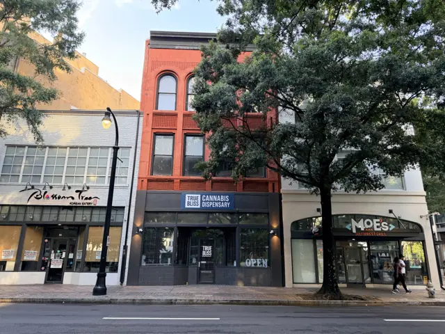 The three-story red brick building at 66 Peachtree Street today, storefronts at the sidewalk and a tree in front.